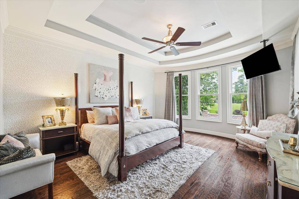 The primary bedroom suite is a retreat all its own, privately located in its own wing. A double tray ceiling and panoramic view through the wall of windows add architectural interest while the wallpapered accent wall adds whimsy to this beloved sanctuary.