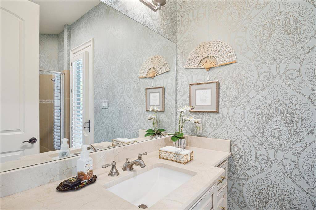 Charmingly sophisticated, this magnificent en-suite bath is luxuriously finished with premium fixtures and soothing wallpaper. The French door provides natural light and private access to the pool.