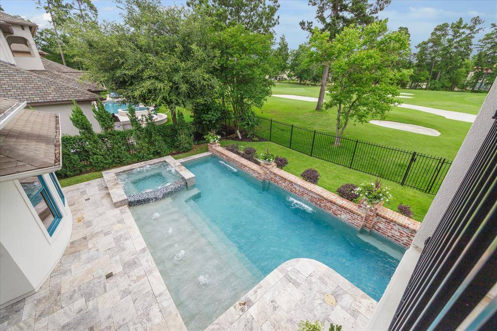 A fantastic view of the resort-style pool and spa surrounded by the lush green landscape of the yard and golf course from the rear balcony.