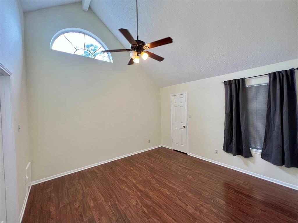 Bedroom 1 with ceiling fan and vaulted ceiling. Light saturates the space through the half moon-shaped window.