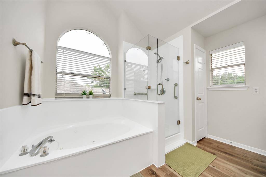 This gorgeous ensuite bathroom showcases a mud-set shower with frameless glass for a sleek, modern touch and effortless access. Natural light pours in through the windows, filling the space with warmth, while the elegant soaking tub offers the perfect spot to unwind and relax.