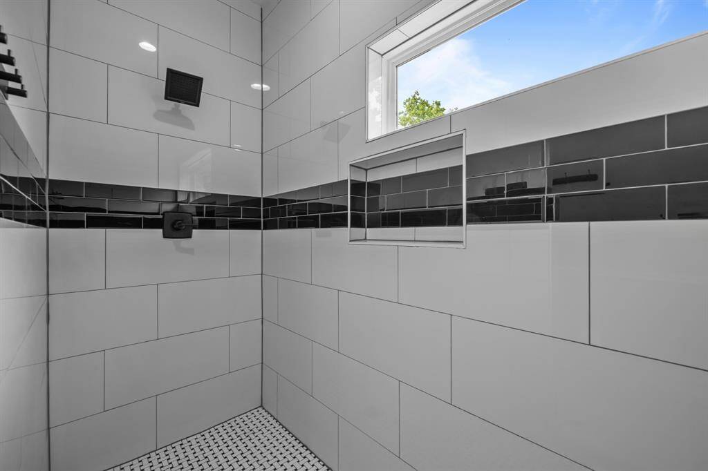 The luxurious, fully tiled walk-in shower showcases a sleek modern design, accented by a shower window, contemporary tile selections, and stylish fixtures.