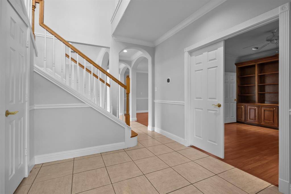 Step into a welcoming foyer featuring arched doorways, detailed crown molding, a stylish half bath, and a French door study with impressive built-ins.