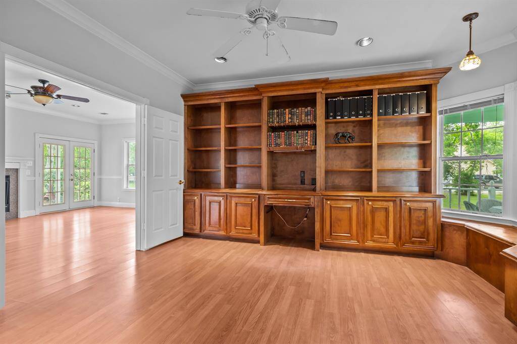 The study features custom built-ins, elegant crown molding, French doors from both the main entrance and living room, a cozy bay window with bench seating, and recessed lighting for a warm, refined feel.