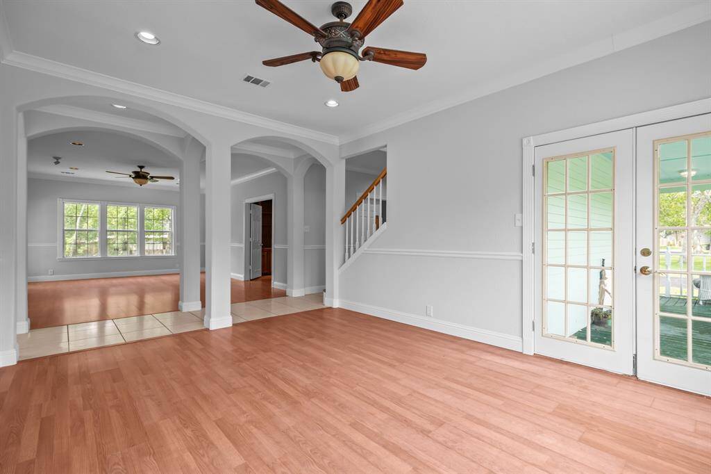 Fresh interior paint highlights elegant details throughout, including chair railing, crown molding, arched doorways, and glass French doors that open to the covered front patio.