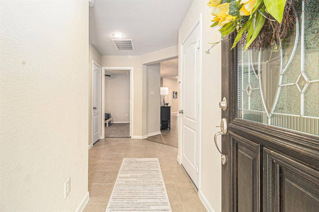Welcoming entryway with neutral tones, tile flooring, and a decorative glass front door.