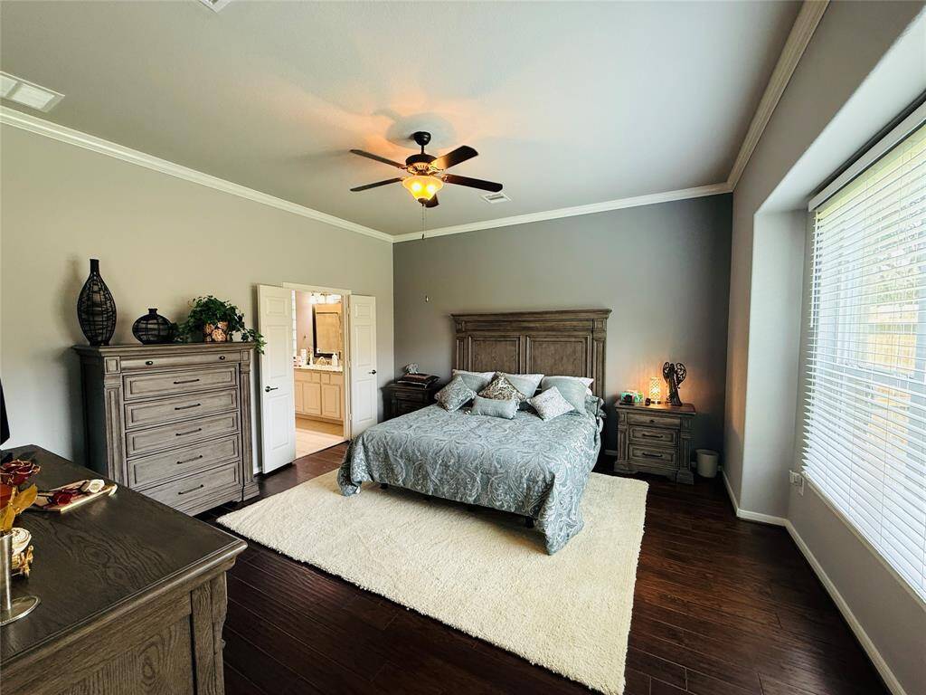 A vast primary bedroom features gleaming engineered hardwood floors, a ceiling fan, and an ensuite bathroom.