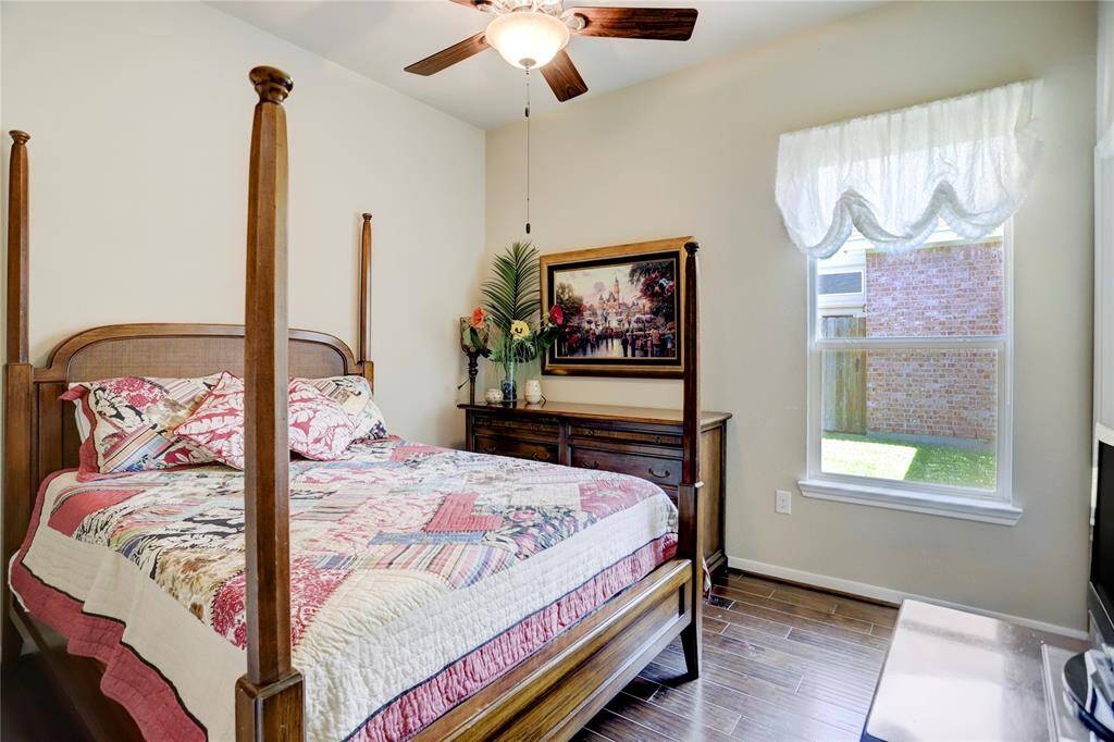 The middle secondary bedroom features a ceiling fan, hardwood flooring, and is well-lit with a warm ambiance.