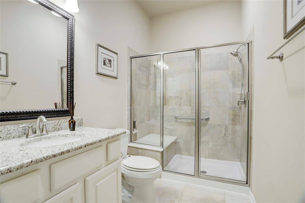 The secondary bathroom features a glass, walk-in shower with a large bench seat and stainless steel handles.