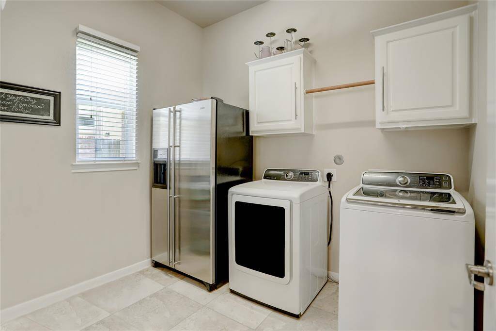 The laundry room is notably spacious, including room for side-by-side, full-sized washer and dryer as well as room for a large side-by-side refrigerator. Above the washer and dryer are white storage cabinets and a closet rod for hang drying. Not pictured is a wall-mounted table for sorting and folding clothes.