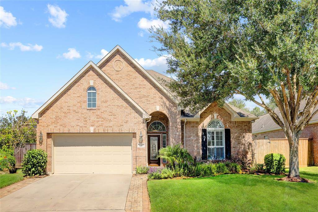 This single-story brick home features a two-car garage, arched windows, and well-manicured landscaping.