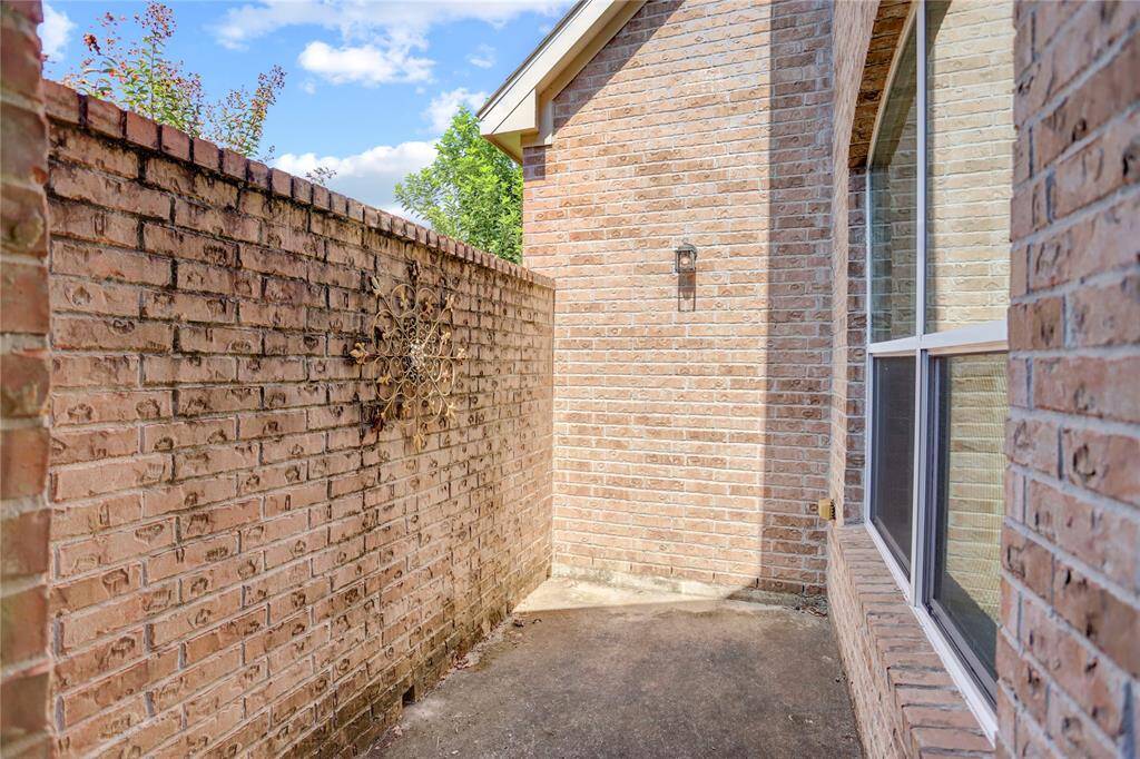This is a side patio, accessible via the study, features a tall privacy brick wall and the side of a brick home with large windows, potentially offering a private outdoor space with a decorative touch.