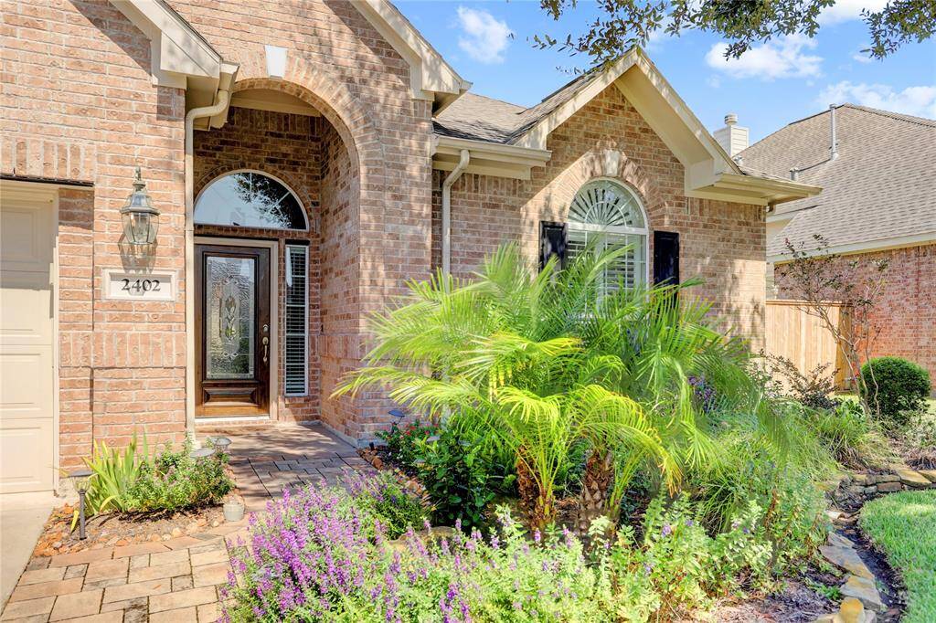 A charming arched entryway, decorative glass front door, and well-maintained landscaping with mature plants.