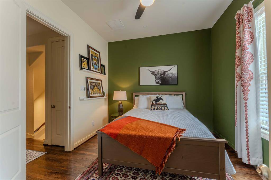 Cozy bedroom featuring a green accent wall, wood flooring, a large window with patterned curtains, and a ceiling fan for comfort.  Complete with an ensuite making it an ideal bedroom.