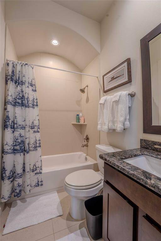 The ensuite features a bullnosed arch above a tub-shower combo and includes a granite countertop, dark wood vanity, and neutral tile flooring. The space is well-lit with recessed lighting and has a towel rack and a small shelf for toiletries.