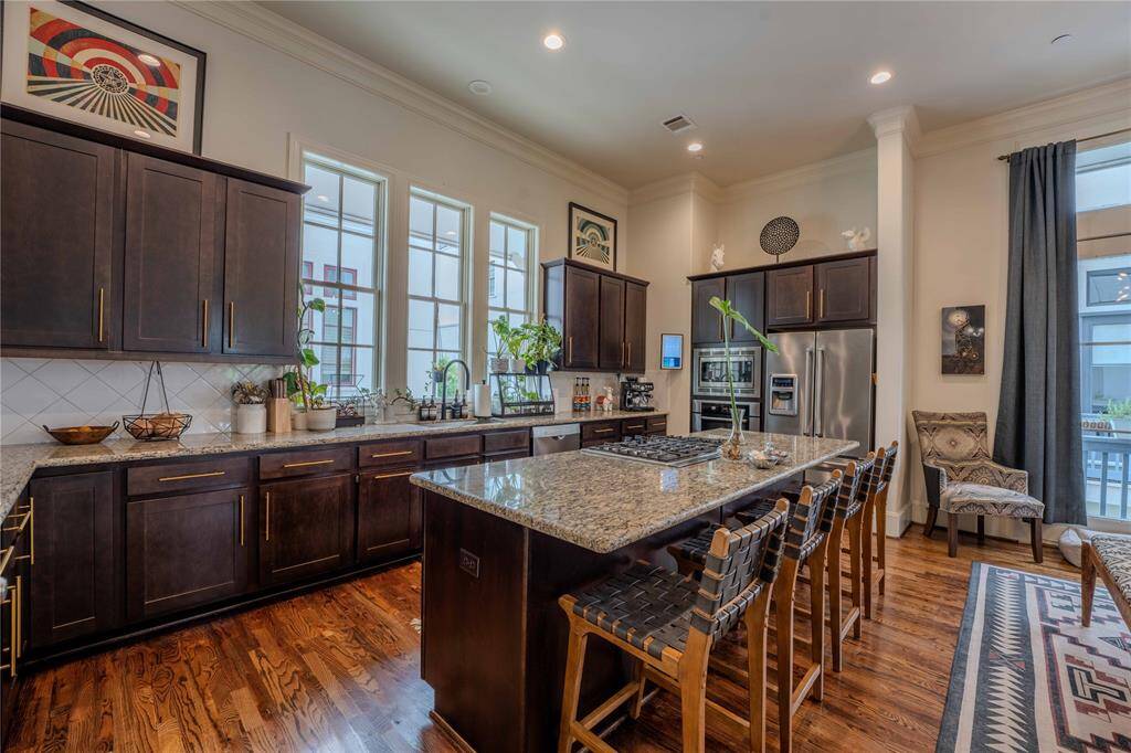 This kitchen is a chef's dream, with rich dark wood cabinets, sleek gold hardware, classic granite counter tops, and an extensive central island with a gas cook top. Stainless steel appliances, ample natural light, and recessed lighting enhance the warm, inviting atmosphere.