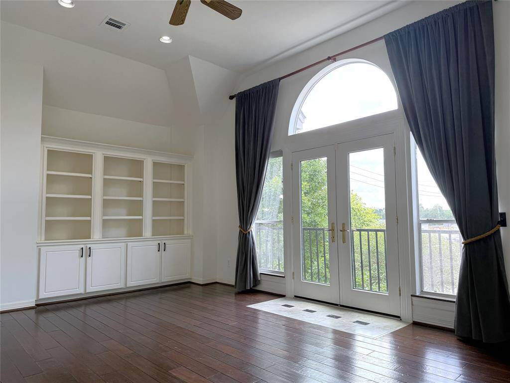 The primary bedroom offers built-in shelving/cabinets. Under the glass paned arch, French doors open in from the standing balcony.