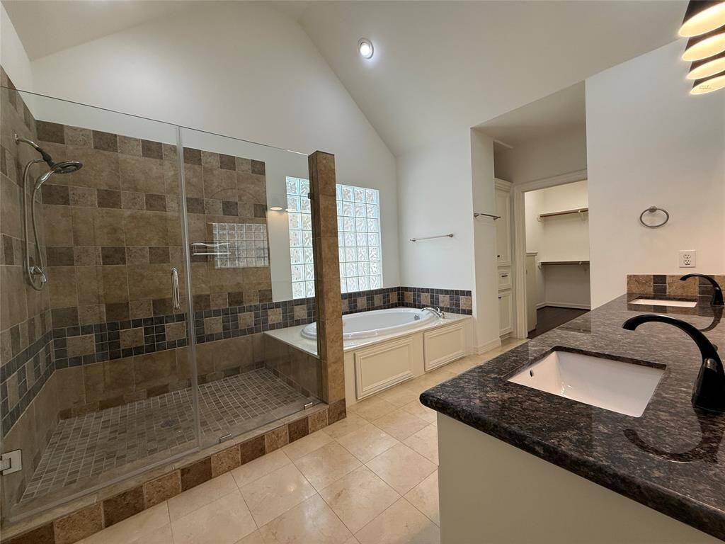 The primary bathroom offers a jetted tub, glass framed shower, twin sink vanity, and two walk-in closets.