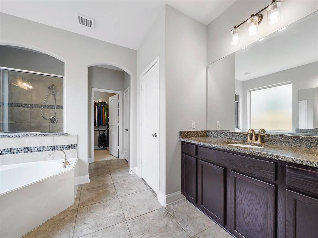 Indulge in the spa-like ensuite bathroom, featuring dual vanities with sinks, a luxurious soaking tub, and a separate walk-in shower. Your private oasis awaits.