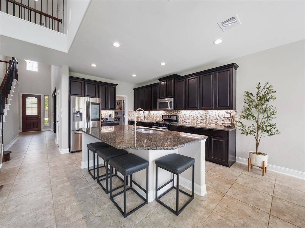 This property features a stunning gourmet island kitchen, equipped with a large island, granite countertops, a tile backsplash, under-cabinet lighting, and stainless steel appliances. This kitchen is designed for both functionality and style.