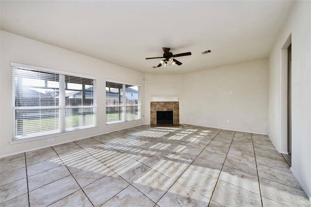 Bright, spacious living room with large windows, tile flooring, and a cozy corner fireplace. Ceiling fan provides added comfort. Ideal for relaxation and entertaining.
