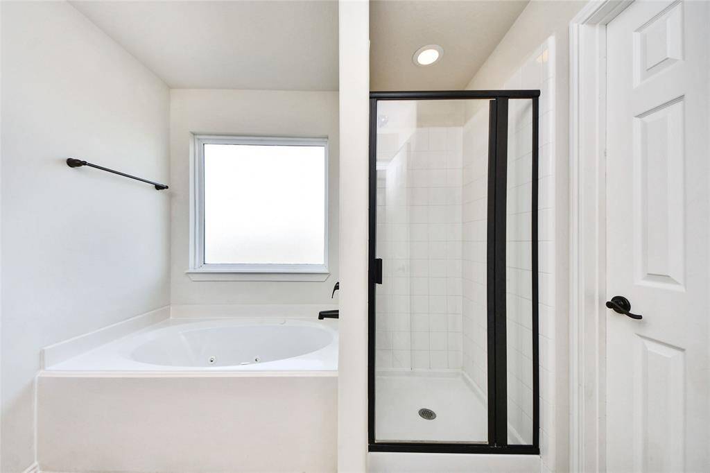 This bathroom features a clean, modern design with a spacious soaking tub and a separate glass-enclosed shower. The space is bright and inviting, thanks to a large frosted window that provides privacy while allowing natural light.