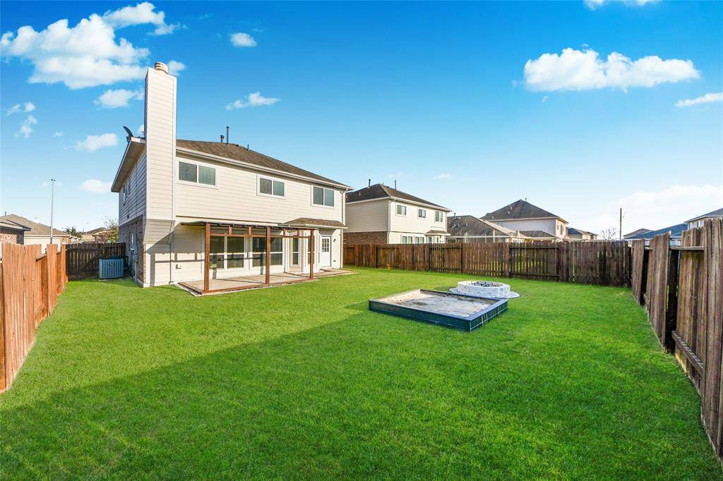 Spacious backyard with a well-maintained lawn, enclosed by a wooden fence. The house features a two-story design with a covered patio, perfect for outdoor relaxation or entertaining.