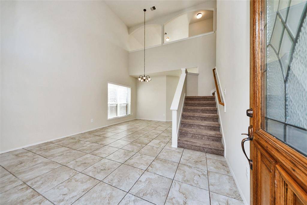 Bright and spacious entryway with high ceilings, tiled flooring, and a staircase leading to the second floor. A large window provides natural light, and there's a stylish hanging light fixture.