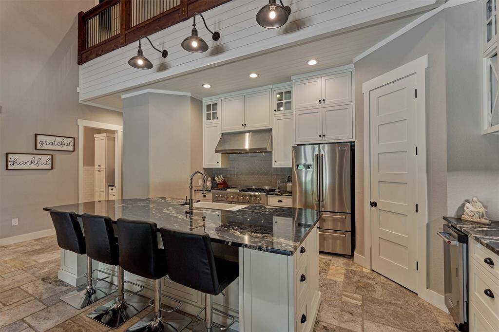 A closer look at the kitchen highlights custom cabinetry crafted specifically for this home, featuring soft-close drawers and doors for added convenience. Farmhouse-style lighting enhances the space above the bar, while a slatted wood accent wall adds warmth and character to the space.