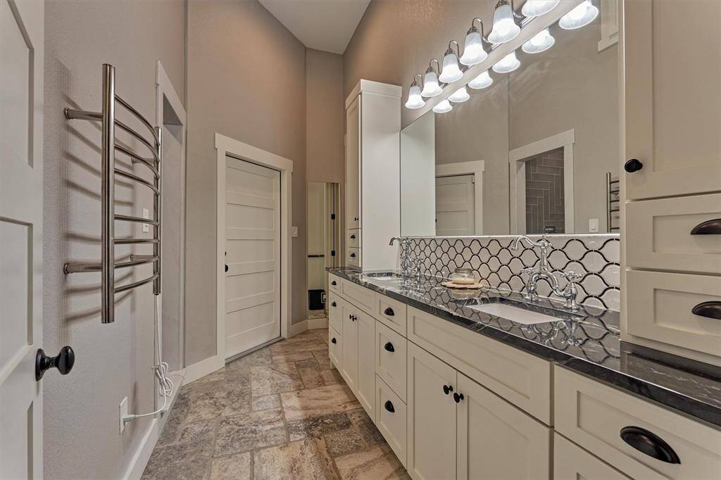 The primary bath is full of custom features such as a unique tile backsplash, cabinetry, towel warmer and access to the home gym and laundry room.