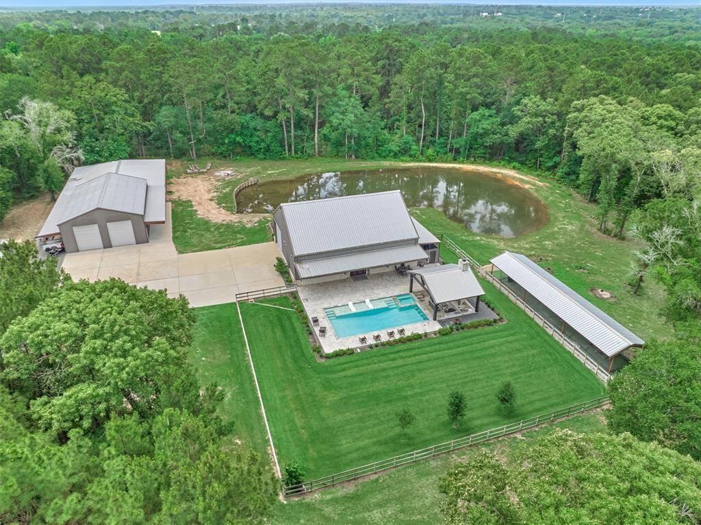 The aerial view shows the custom barndominium-style home, oversized shop, sparkling chlorine pool, fenced area, and a private batting cage- perfect for active living and hosting in a serene setting.