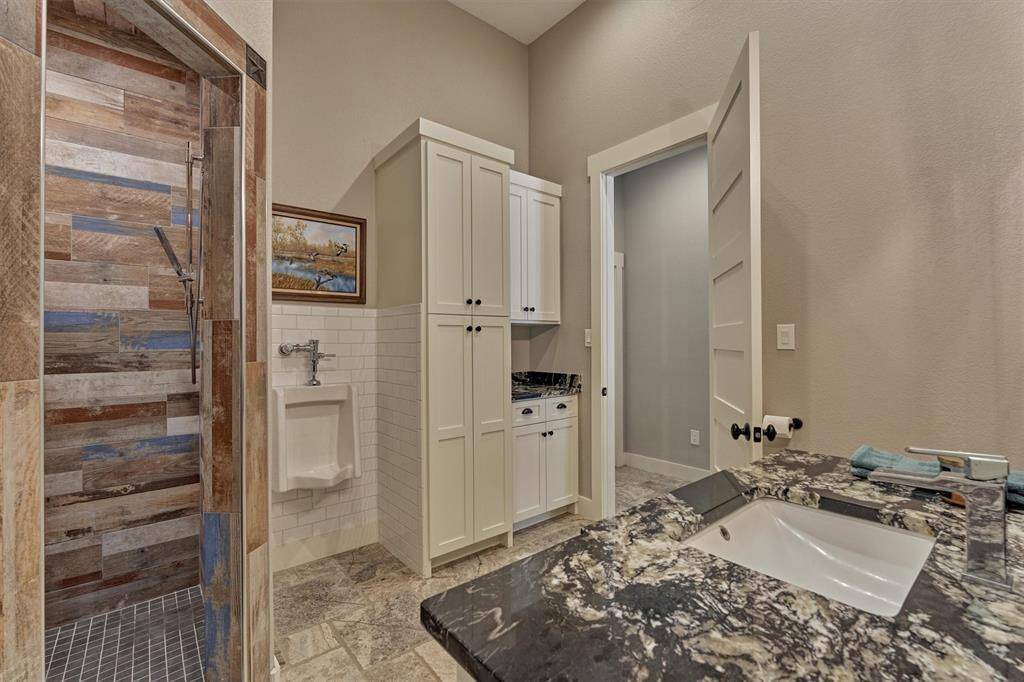 Another view of this well-appointed bath reveals abundant storage, a separate urinal, and a walk-in shower accented with wood-look tile that enhances the rustic charm.
