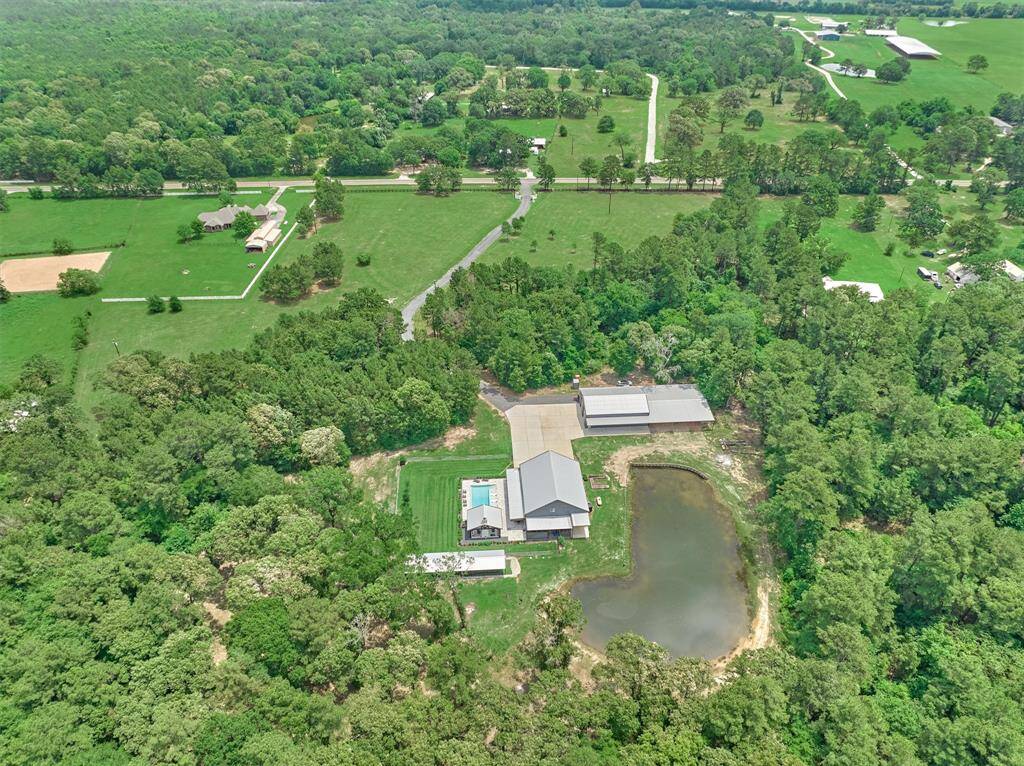 This aerial view of the property looking toward the main road reveals a natural buffer of mature trees, offering a secluded and private setting for the home.