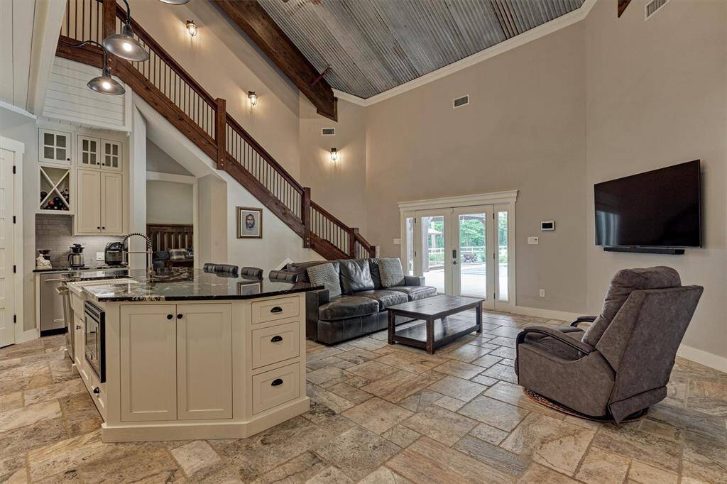 The rustic yet refined aesthetic carries through with a metal ceiling and cedar-lined staircase, adding warmth and character to the space. Double glass doors offer a beautiful view of the pool area and expansive yard, bringing the outdoors in.