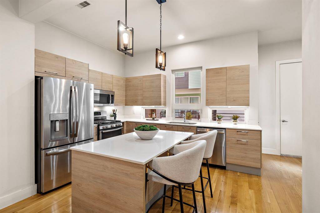 Stainless steel appliances, a gas range, and modern pendant lights elevate the space, while elevated windows and balcony access keep the area light and inviting.
