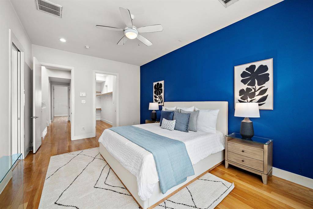 Primary suite showcases a bold blue accent wall, hardwood floors, and enough space for a king-size bed with additional furnishings.