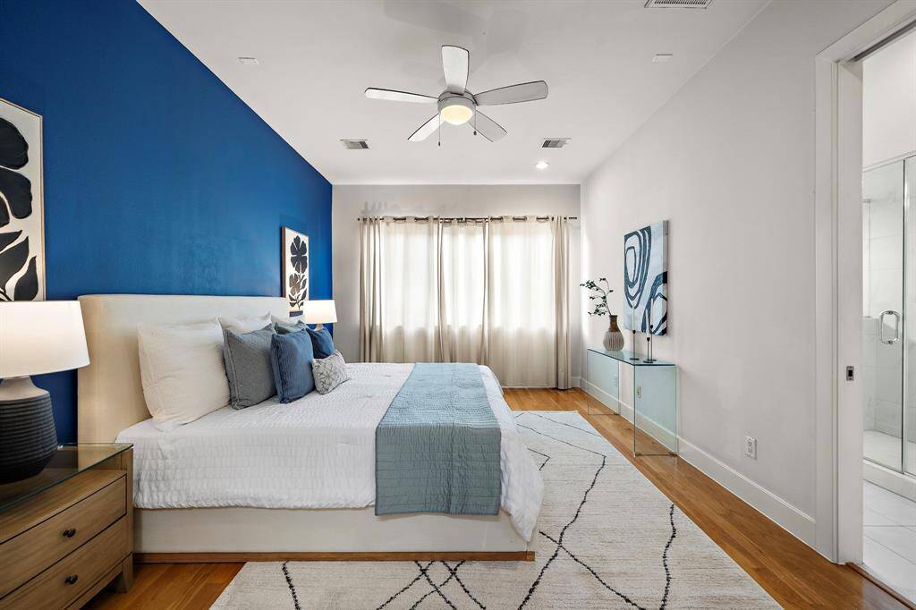 Primary suite features a striking blue accent wall, hardwood flooring, and an abundance of natural light from large windows.