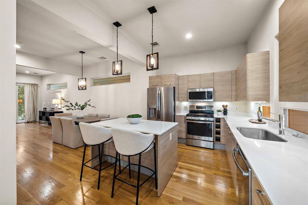 Contemporary kitchen features an oversized island with bar seating, sleek stainless appliances including a gas range, and modern light-hued cabinetry.