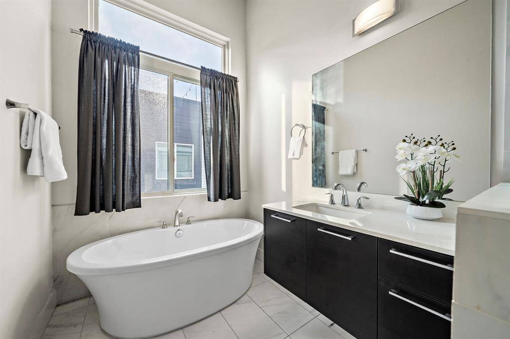 Sleek primary bath features a freestanding soaking tub set beneath an expansive window, offering a tranquil spot to unwind.