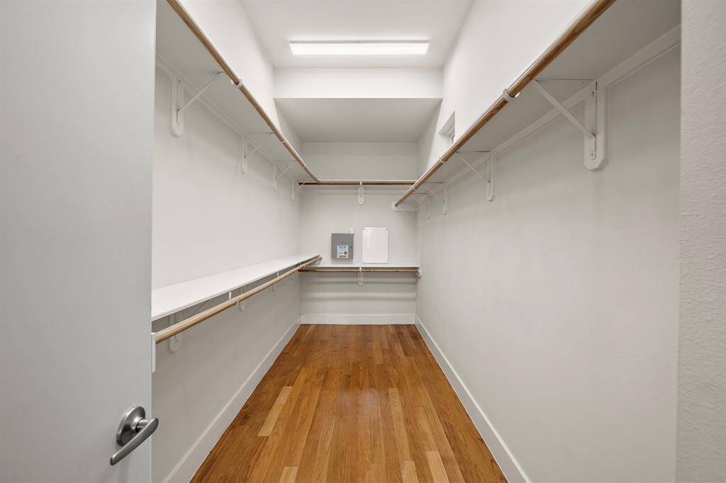 Expansive walk-in closet in the primary suite features dual-level hanging rods, hardwood floors, and custom shelving for streamlined organization.