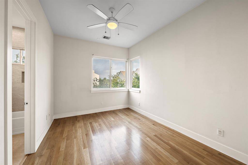 Secondary bedroom features hardwood floors, a neutral palette, and corner windows that bring in abundant natural light along with neighborhood views.