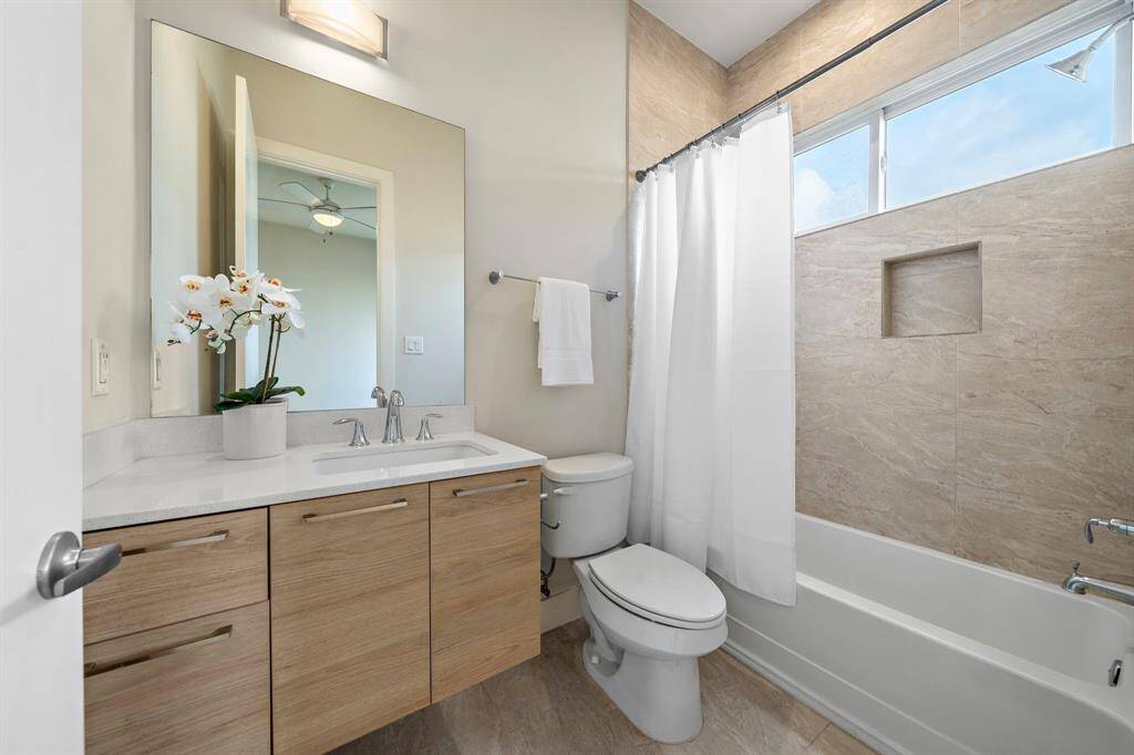 Modern secondary bath features a sleek floating vanity with quartz countertop, an oversized mirror, and contemporary fixtures.