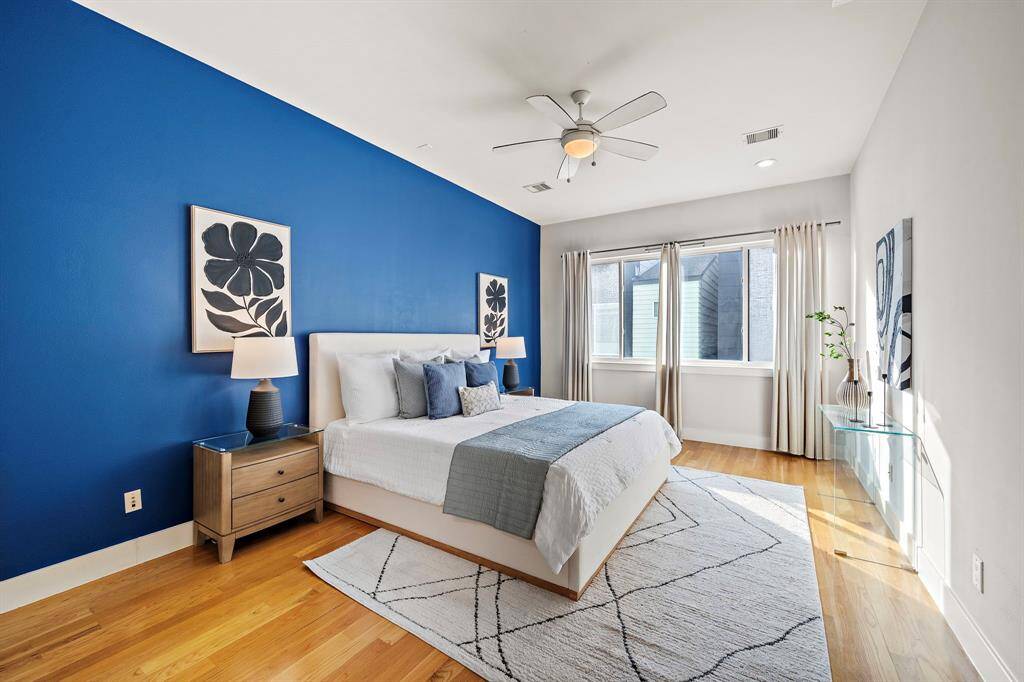 Expansive primary bedroom features a bold accent wall, hardwood floors, and large windows that fill the space with natural light.