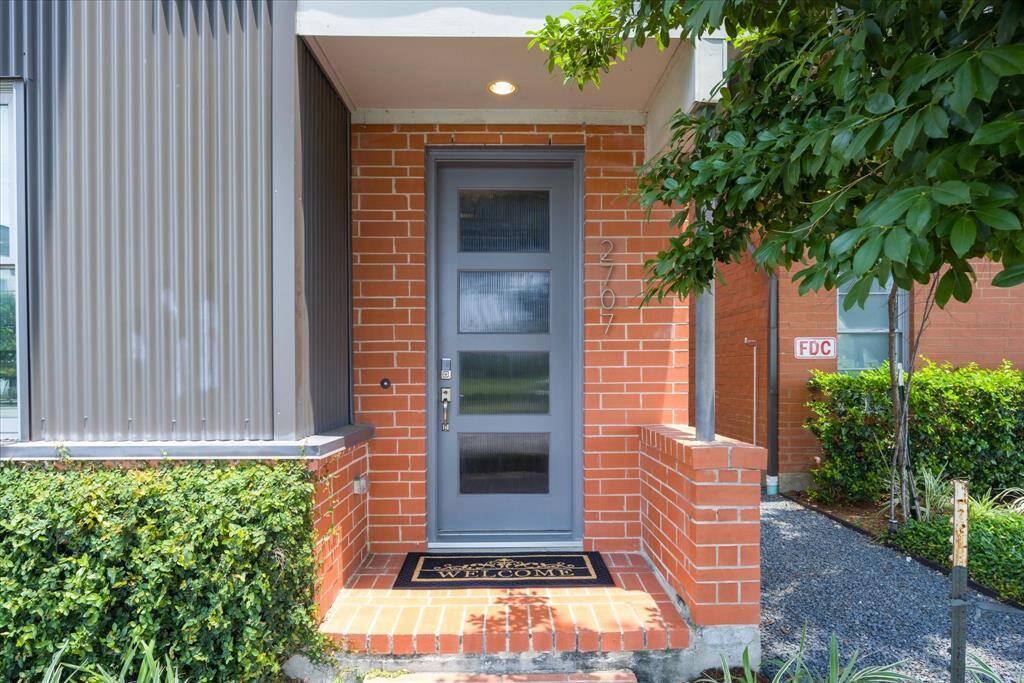 This is your invitation to enjoy luxury living in the heart of Houston. This stylish front entrance sets the tone with a sleek door, rich brick exterior, and lush greenery, offering a warm first impression that perfectly reflects the modern elegance found throughout this stunning townhome.