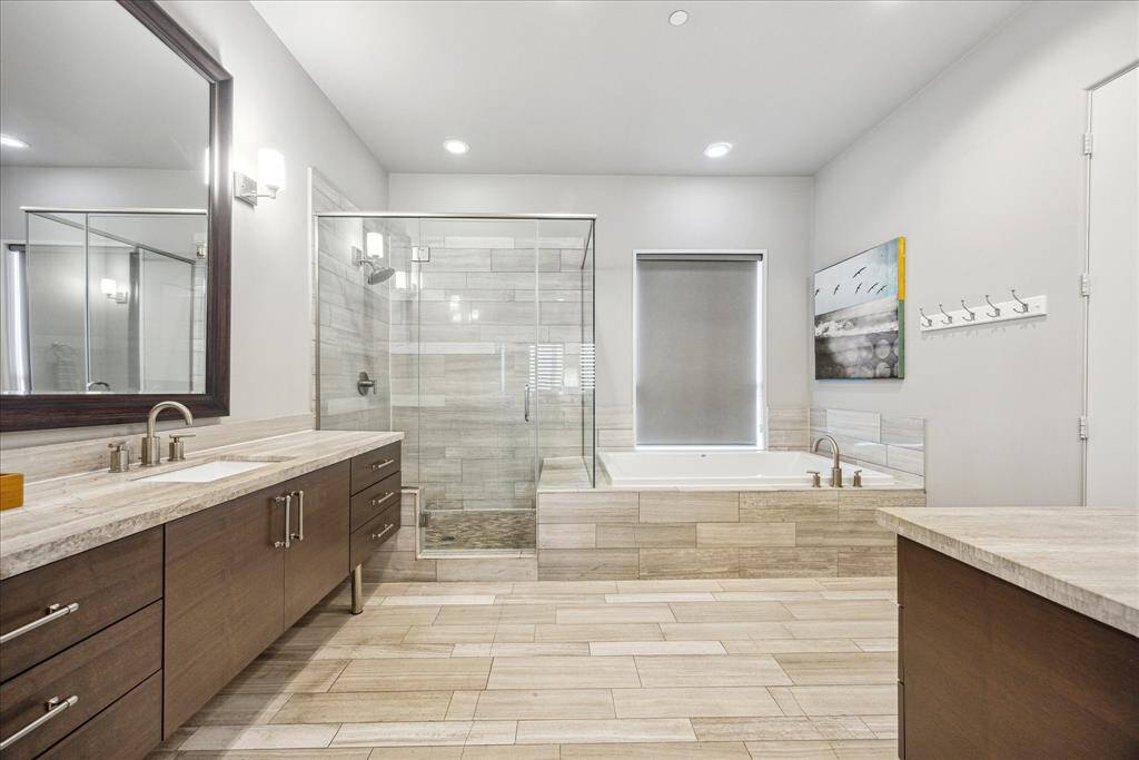 Designed to feel like a private spa, this luxurious en suite bath offers a serene escape with a spacious walk-in glass shower, deep soaking tub, and dual vanities with generous counter space. Sleek wooden cabinetry and soft, neutral tones create a calming atmosphere, perfect for starting or ending the day in comfort and style.