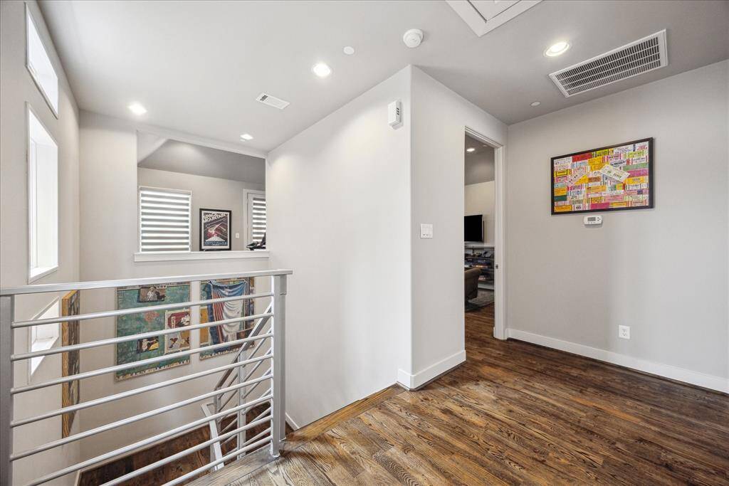 This spacious landing serves as a stylish connector between levels, featuring warm hardwood floors, neutral walls, and sleek recessed lighting. Overlooking the modern staircase with its metal railing, the area is bathed in natural light and offers the ideal space to showcase artwork or create a personalized transition between rooms.