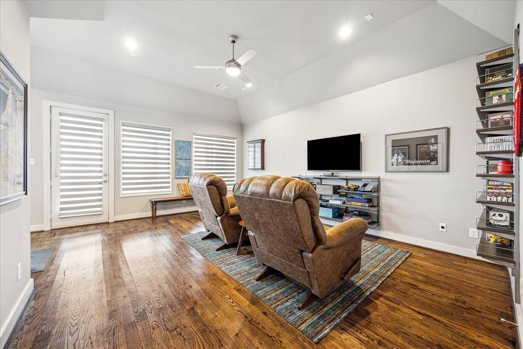 This light-filled room offers flexible living with its spacious layout, high ceiling, and warm hardwood floors. Currently styled as a media or game room, it also functions perfectly as an additional bedroom, complete with a closet, large windows, modern blinds, and built-in shelving for comfort and convenience.