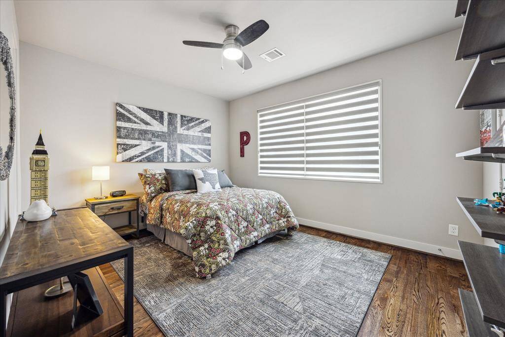This bright and inviting bedroom is the third in the home to feature an en suite bath, which also offers a separate hallway entrance for added flexibility. Thoughtfully designed, the room includes a modern ceiling fan, a large window with custom blinds, and wall-mounted shelving, making it a comfortable and functional space for guests, family, or everyday living.