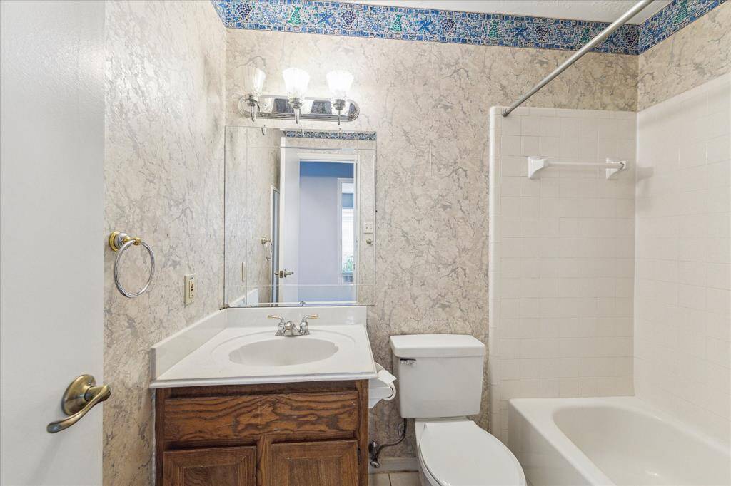 The guest bathroom features a single sink vanity with a beveled mirror and vanity lighting above, plus a fully tiled tub/shower enclosure combining style and function for everyday comfort.