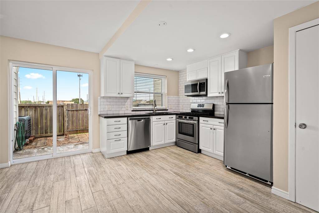 Stylishly updated kitchen featuring white cabinetry, sleek granite countertops, and stainless steel appliances. Subway tile backsplash adds a modern touch, while the sliding glass doors provide natural light and lead to a private outdoor patio